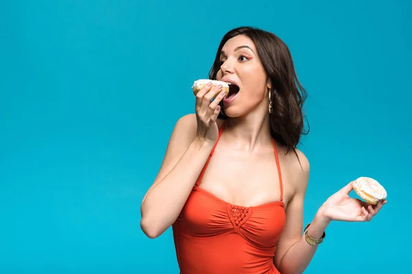 Junge Frau im Badeanzug isst Donut isoliert auf blau — Stockfoto