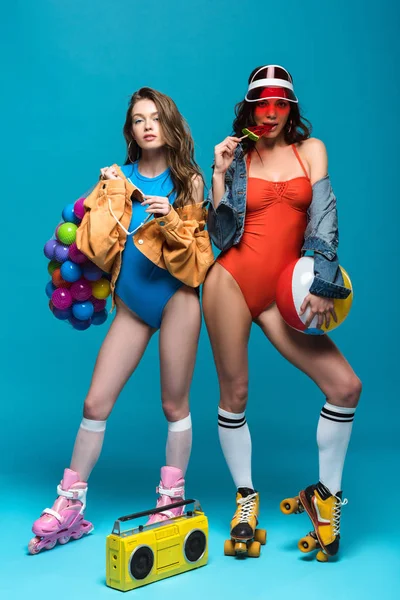 Vista completa de dos chicas elegantes en patines comiendo piruleta de sandía en azul - foto de stock