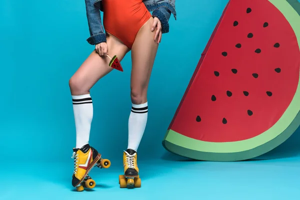 Cropped view of girl in swimsuit and roller skates holding lollipop on blue — Stock Photo