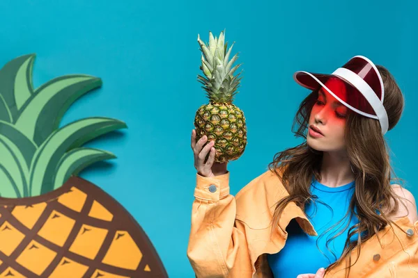 Pensive girl in cap holding pineapple isolated on blue — Stock Photo