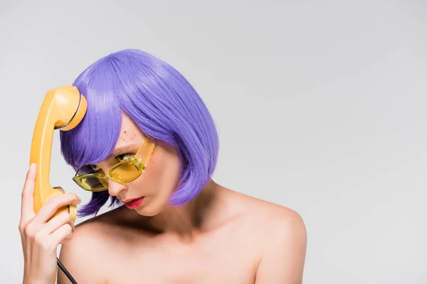 Chica aburrida en peluca púrpura sosteniendo teléfono retro, aislado en gris - foto de stock