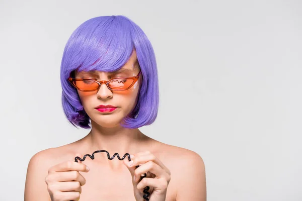 Приваблива дівчина в фіолетовій перуці дивиться на шнур вінтажного телефону, ізольована на сірому — стокове фото