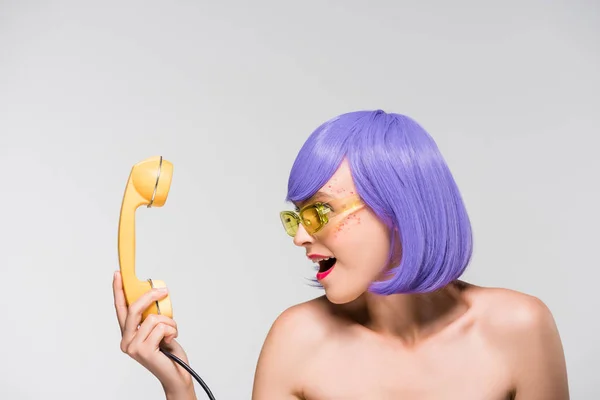 Attraktive Frau mit lila Perücke blickt auf Retro-Telefon, isoliert auf grau — Stockfoto