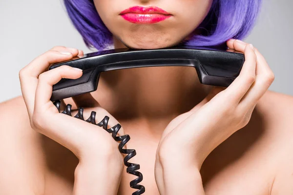 Vista recortada de chica molesta en peluca púrpura sosteniendo teléfono retro, aislado en gris - foto de stock