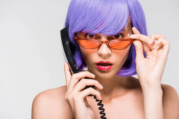 Шокированная женщина в фиолетовом парике держит ретро-телефон, изолированный на сером — стоковое фото