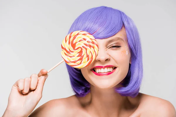 Cheerful girl in purple wig holding sweet lollipop, isolated on grey — Stock Photo