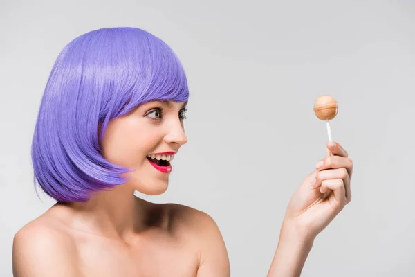 Chica con estilo en peluca púrpura celebración de piruleta dulce, aislado en gris - foto de stock