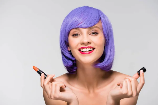 Hermosa chica en púrpura peluca celebración de lápiz labial aislado en gris - foto de stock