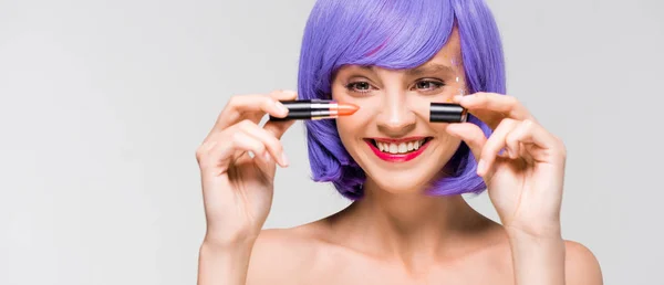 Happy girl in purple wig holding lipstick isolated on grey — Stock Photo