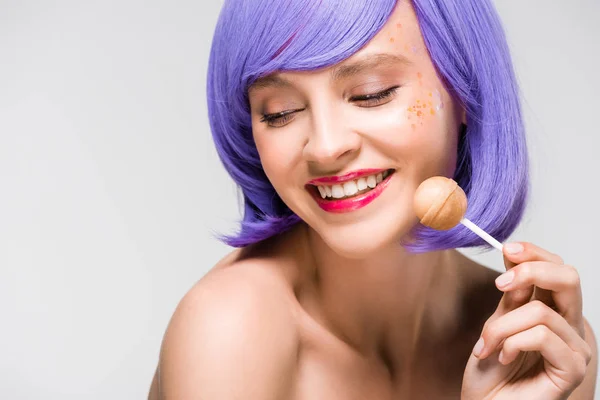 Chica desnuda sonriente en peluca púrpura sosteniendo dulce piruleta, aislado en gris — Stock Photo