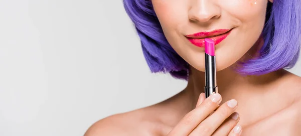 Cropped view of girl in purple wig holding lipstick isolated on grey — Stock Photo