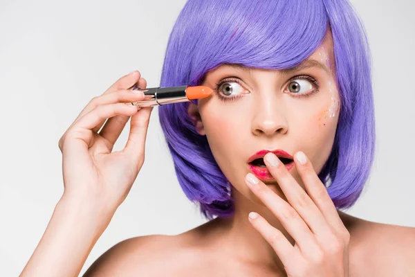 Élégante fille choquée en perruque violette tenant rouge à lèvres isolé sur gris — Photo de stock