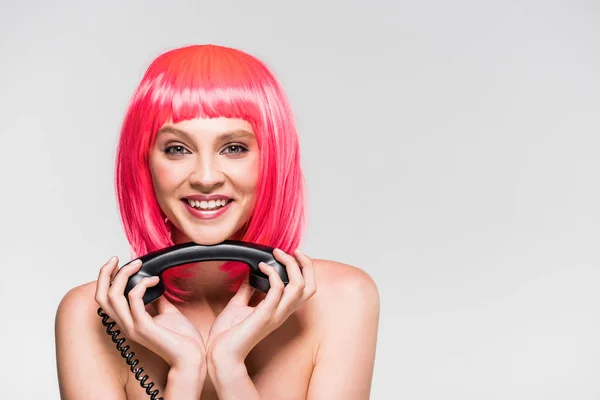Симпатичная улыбающаяся девушка в розовом парике с винтажным телефоном, изолированная на сером — стоковое фото