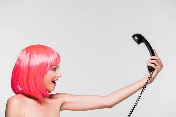 Beautiful woman in pink wig looking at retro telephone, isolated on grey — Stock Photo