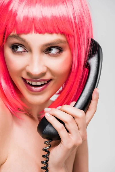Красива усміхнена жінка в рожевій перуці говорить на ретро телефоні, ізольована на сірому — стокове фото