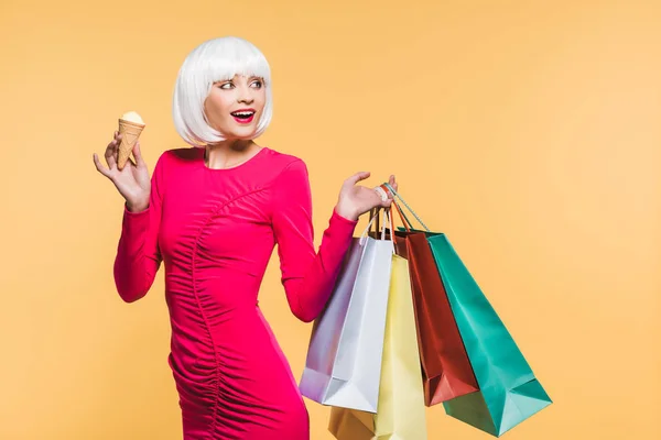 Cheerful girl in white wig with shopping bags and ice cream, isolated on yellow — Stock Photo