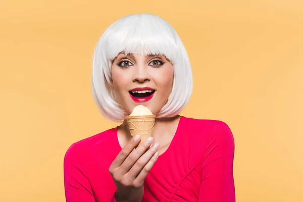 Усміхнена жінка в білому перуці їсть морозиво, ізольована на жовтому — стокове фото