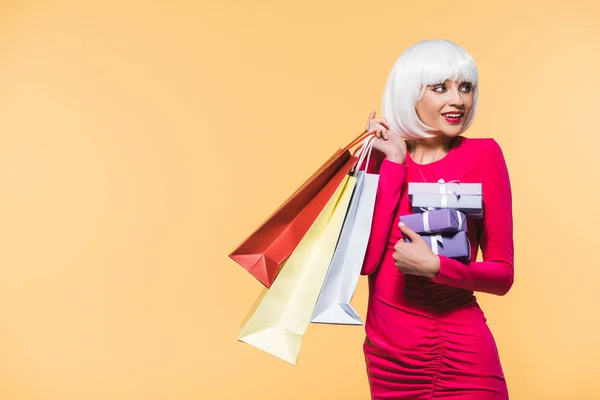 Atractiva mujer con regalos y bolsas de compras, aislado en amarillo - foto de stock