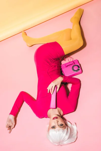 Вид зверху на стильну привабливу жінку в білому вігві з ретро телефоном на рожевому — стокове фото