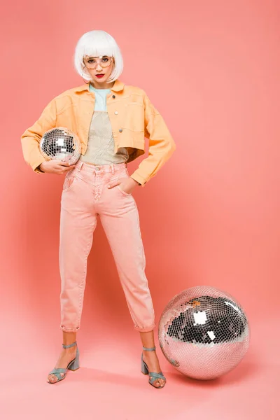 Elegante chica en peluca blanca posando con bolas de discoteca en rosa - foto de stock