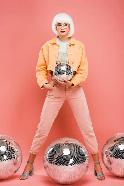 Hermosa chica de moda en peluca blanca posando con bolas de discoteca en rosa - foto de stock