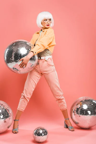 Mujer de moda en peluca blanca posando con bolas de discoteca en rosa - foto de stock