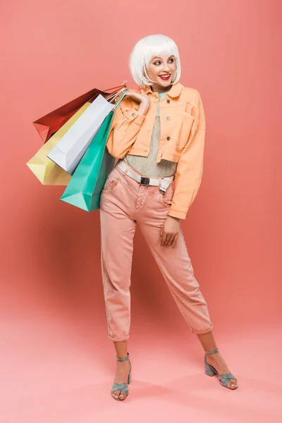 Atractiva chica sonriente en peluca blanca con bolsas de compras en rosa - foto de stock