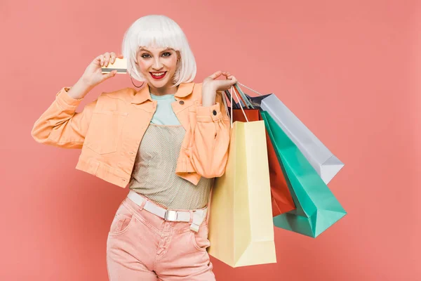 Jolie fille en perruque blanche avec des sacs à provisions et carte de crédit, isolé sur rose — Photo de stock