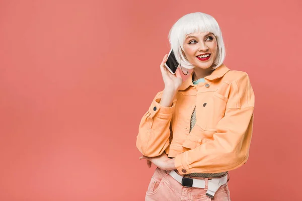 Atractiva mujer sonriente hablando en el teléfono inteligente, aislado en rosa - foto de stock
