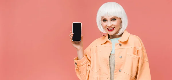 Chica sonriente mostrando teléfono inteligente con pantalla en blanco, aislado en rosa - foto de stock