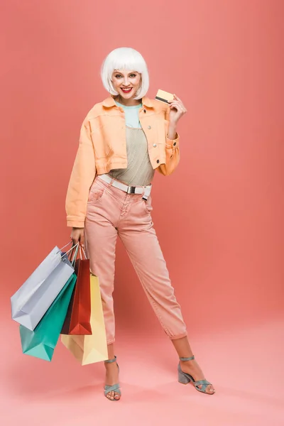 Fille heureuse en perruque blanche avec des sacs à provisions et carte de crédit sur rose — Photo de stock