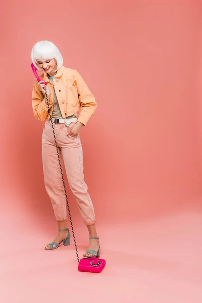 Beautiful fashionable woman in white wig talking on vintage telephone on pink — Stock Photo