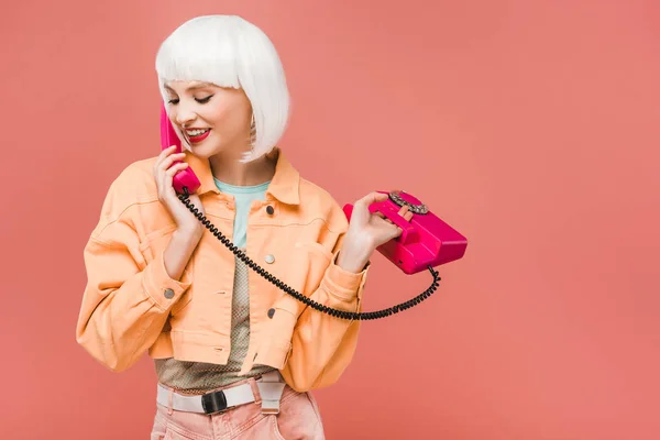 Smiling girl in white wig talking on retro telephone, isolated on pink — Stock Photo