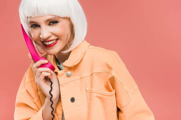 Felice donna elegante in parrucca bianca parlando al telefono vintage, isolato su rosa — Foto stock