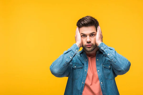 Impactado hombre guapo con las manos en la cabeza aislado en amarillo con espacio de copia - foto de stock