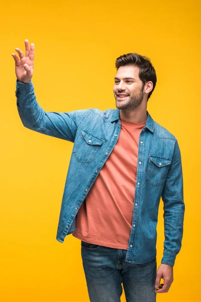Hombre guapo gesticulando con la mano y sonriendo aislado en amarillo - foto de stock