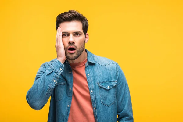 Scioccato bello uomo toccare il viso e guardando la fotocamera isolata su giallo — Foto stock