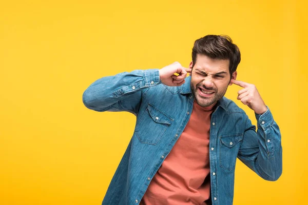 Dissatisfied handsome man plugging ears with fingers isolated on yellow — Stock Photo