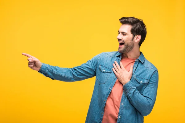 Homem bonito rindo e apontando com o dedo isolado no amarelo — Fotografia de Stock