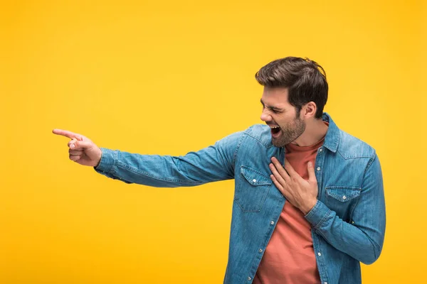 Handsome man laughing and pointing with finger isolated on yellow — Stock Photo