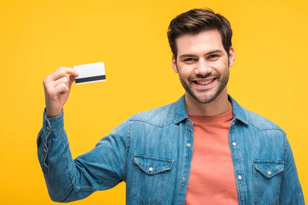 Guapo sonriente hombre sosteniendo tarjeta de crédito aislado en amarillo - foto de stock
