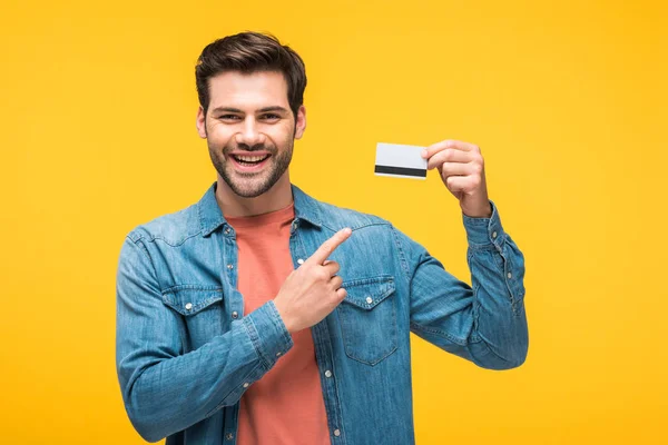 Hombre guapo señalando con el dedo a la tarjeta de crédito aislado en amarillo - foto de stock