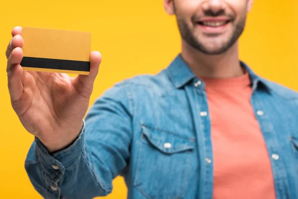 Обрезанный вид человека, держащего кредитную карту с копировальным пространством, изолированным на желтый — стоковое фото