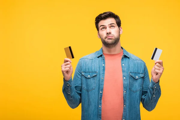 Confus beau homme tenant des cartes de crédit isolé sur jaune — Photo de stock