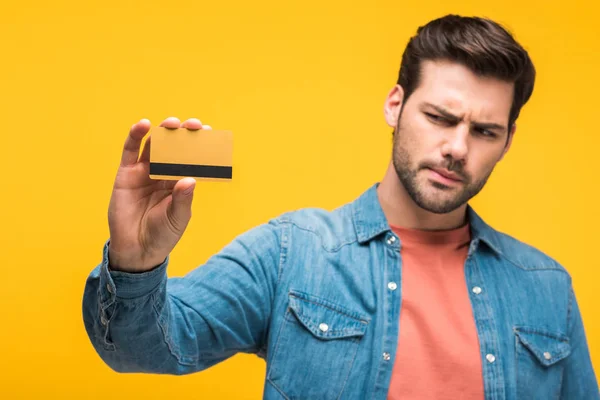 Confused handsome man holding credit card isolated on yellow — Stock Photo
