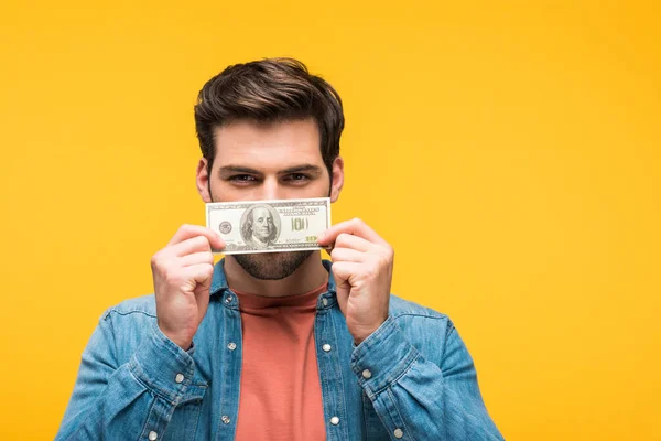 Красивий чоловік вкриває обличчя грошима ізольовано на жовтому — стокове фото