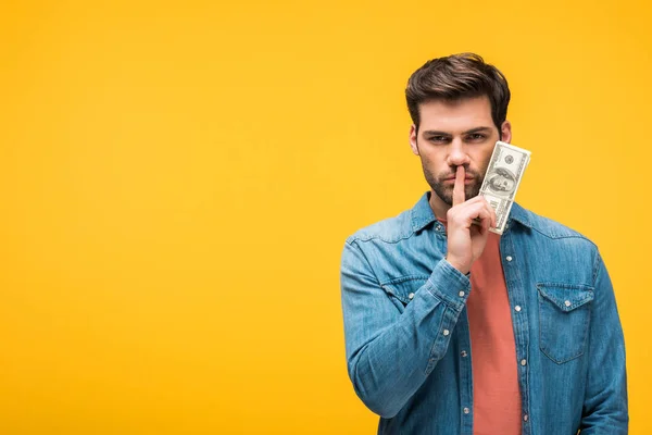 Bonito homem fazendo silêncio gesto e segurando dinheiro isolado no amarelo — Fotografia de Stock