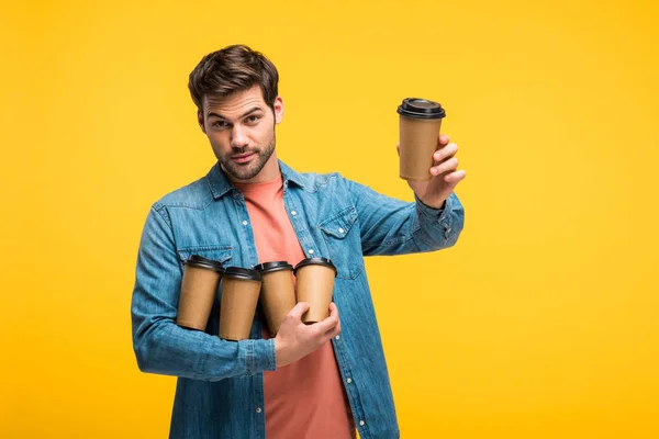 Handsome man holding paper cups and looking at camera isolated on yellow — Stock Photo