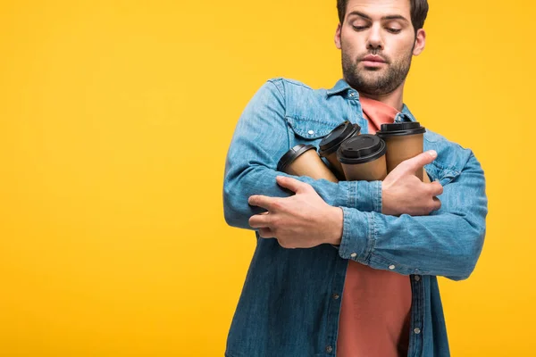 Hombre guapo sosteniendo tazas de papel con café para ir aislado en amarillo - foto de stock