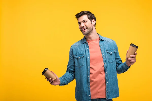 Bell'uomo sorridente che tiene tazze di carta con caffè per andare isolato sul giallo — Foto stock